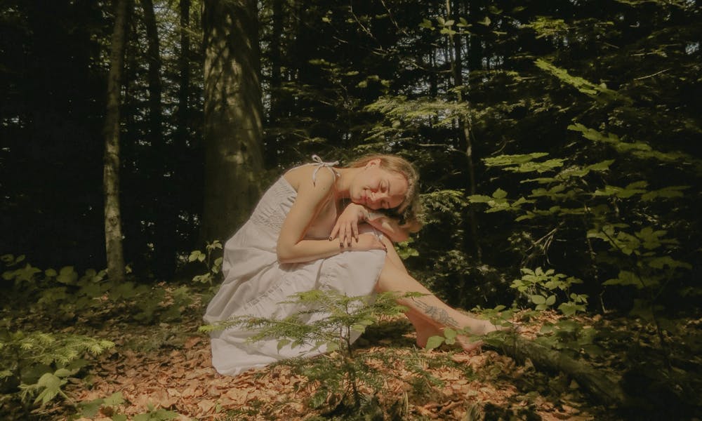 A woman in a white dress is sitting on the ground in the woods .pexels
