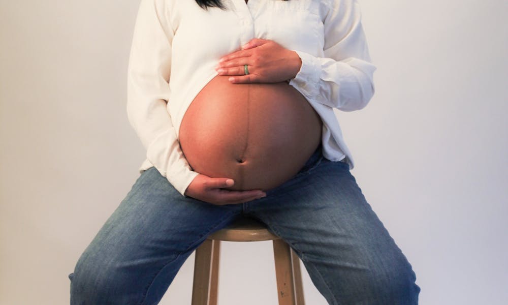 A pregnant woman sitting on a stool in front of a white background .pexels