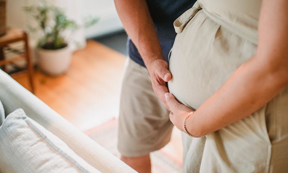 From above of crop faceless couple in casual outfit standing in light living room and touching pregnant belly gently .pexels