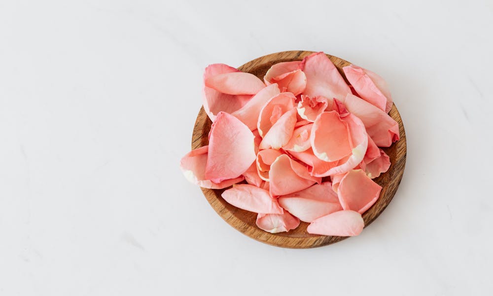 Delicate rose petals and wooden plate on white background .pexels