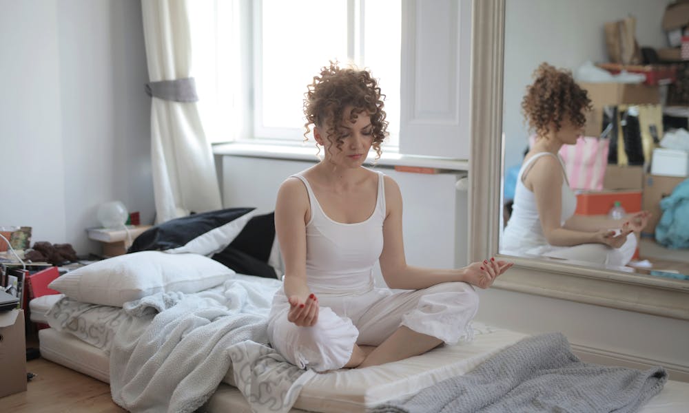 Tranquil female in sleepwear sitting on bed in messy room and practicing yoga with closed eyes while maintaining mental health .pexels