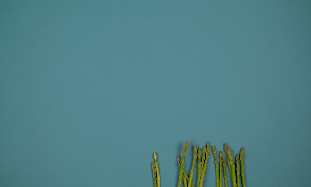 Top view of raw asparagus stalks with ribbed surface in row on green background .pexels