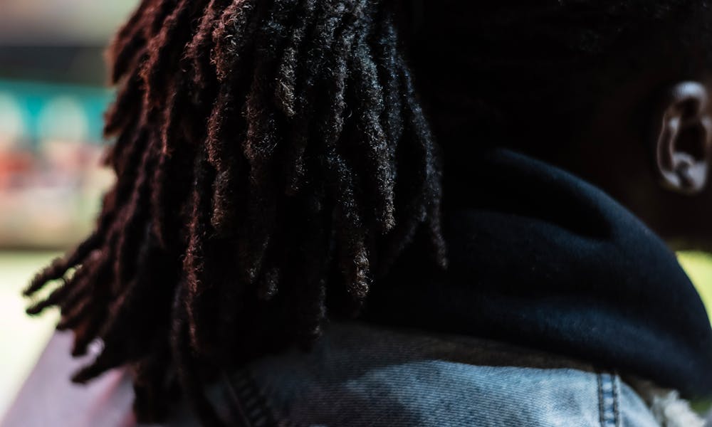 Side view of stylish African American male with black hair wearing denim jacket sitting on street against blurred background in city .pexels