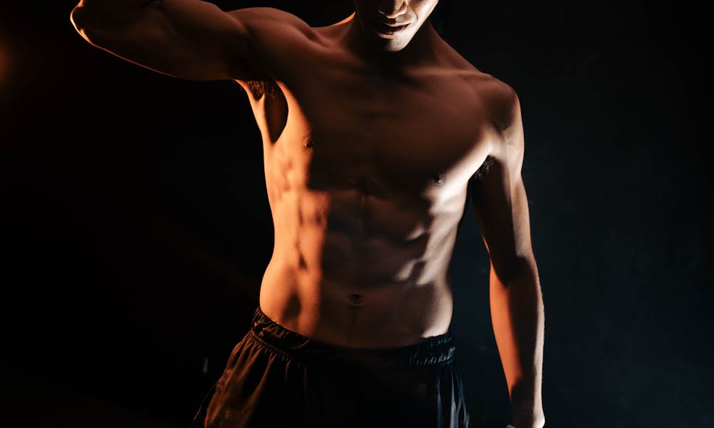 A shirtless man flexing his muscles in the dark .pexels