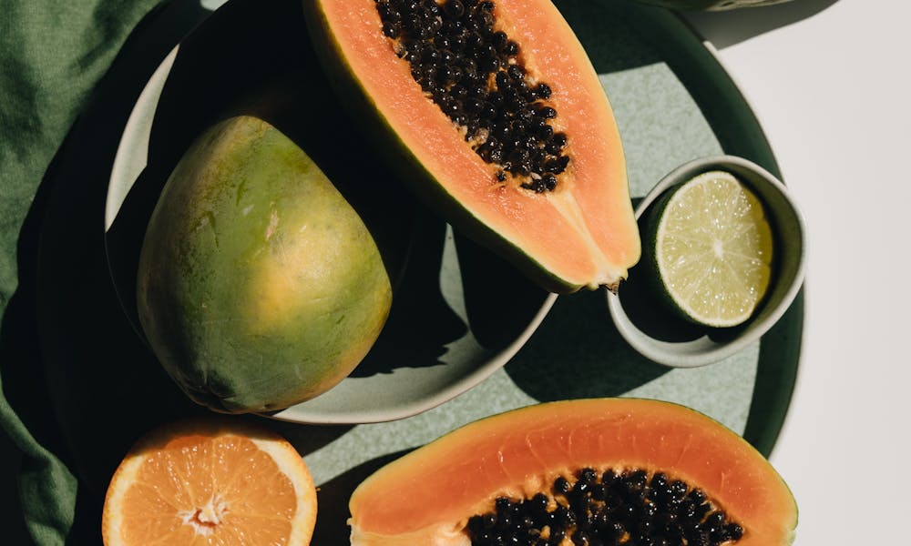 Top view of halves of ripe papaya together with oranges and limes placed on green round dishes and green fabric on white background .pexels