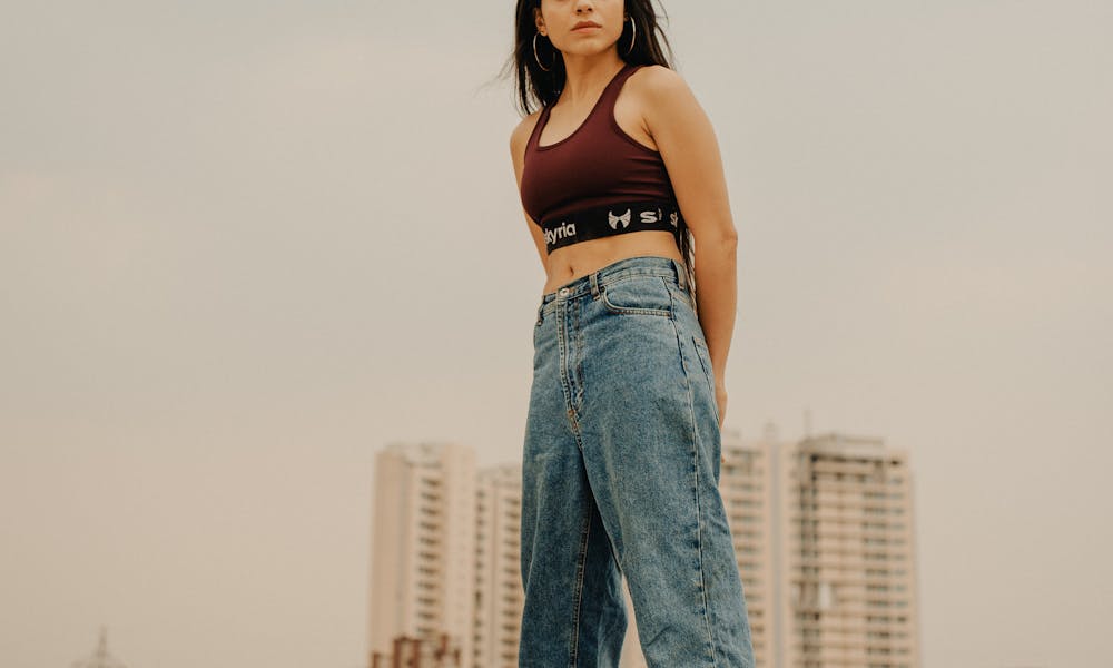 Full body of young female wearing sport top and denim with sneakers standing on rooftop of modern building .pexels