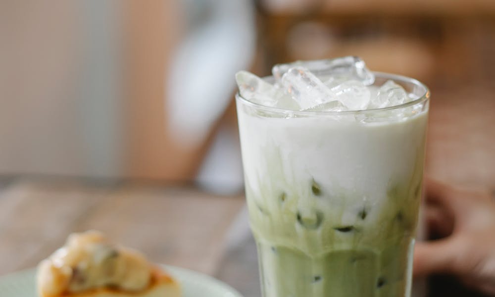 Glass of tasty refreshing matcha latte served on table with yummy pie slice in cafe .pexels