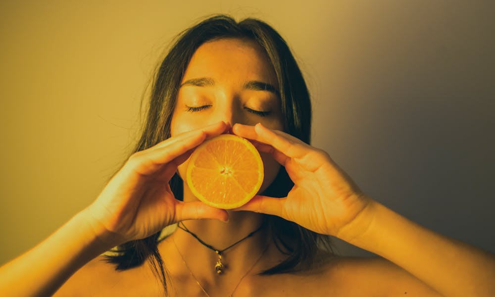 Attractive woman with eyes closed holding orange slice against lips .pexels