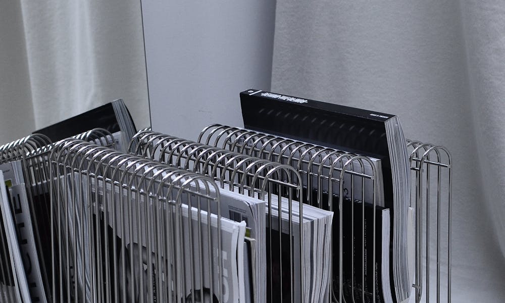 Collection of modern fashion magazines on metal rack placed on floor near mirror and curtain in room corner .pexels