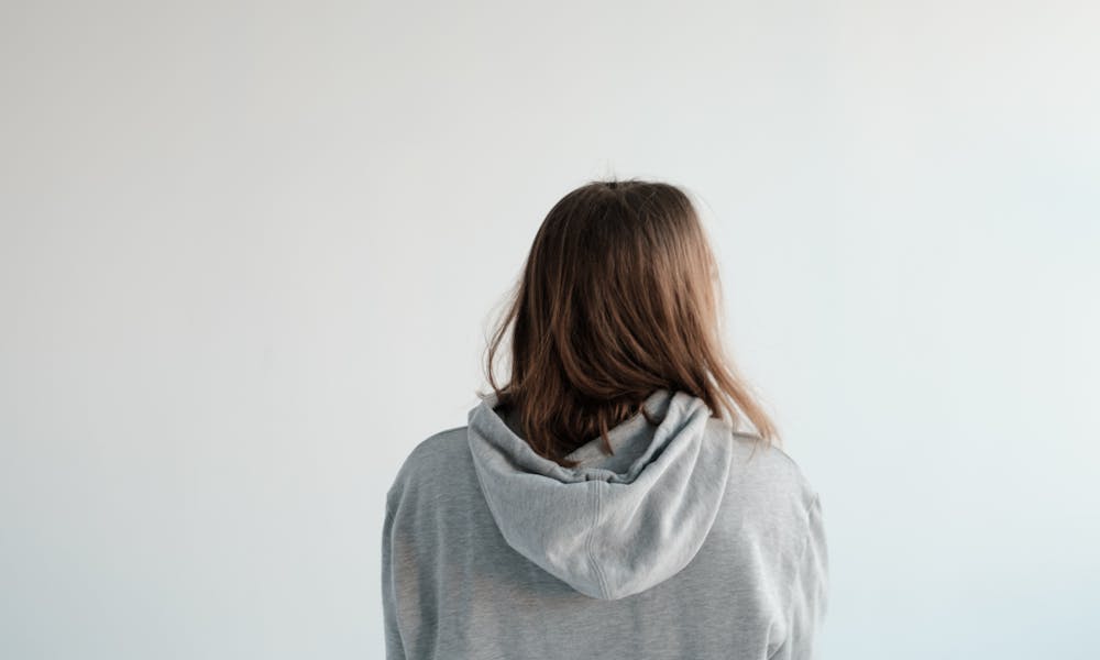 Back view of unrecognizable female with brown hair wearing gray hoodie and denim pants standing on white background in studio .pexels