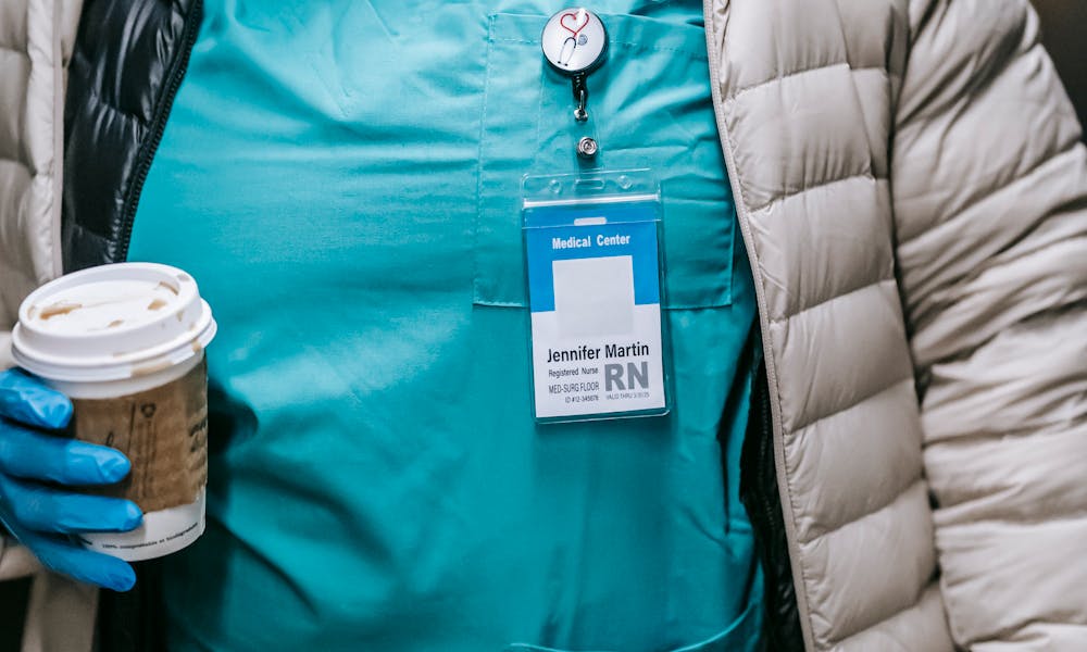 Crop unrecognizable African American nurse in uniform and protective mask wearing warm clothes walking with takeaway coffee in public place .pexels