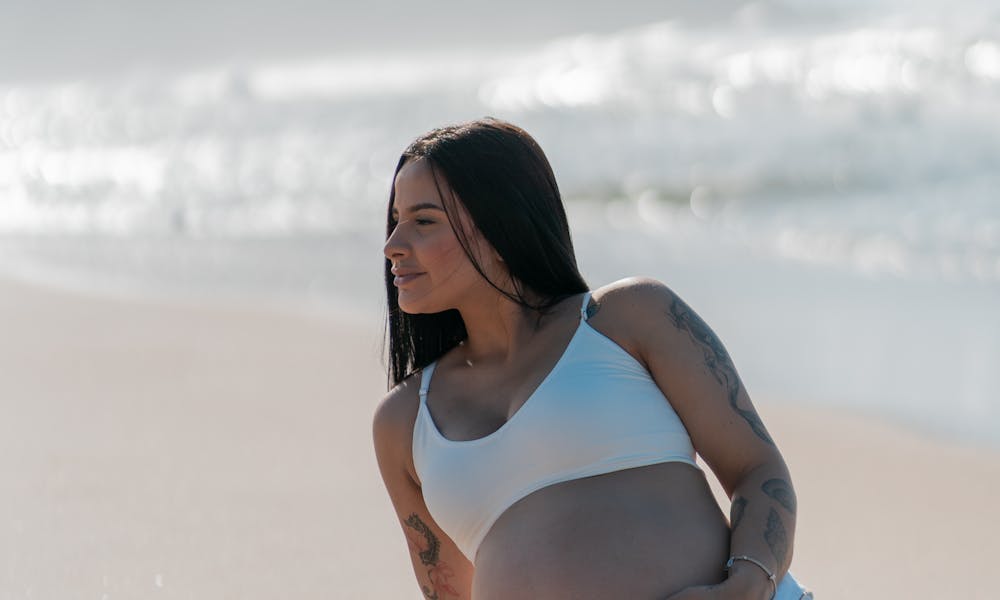 A pregnant woman sitting on the beach with her belly .pexels