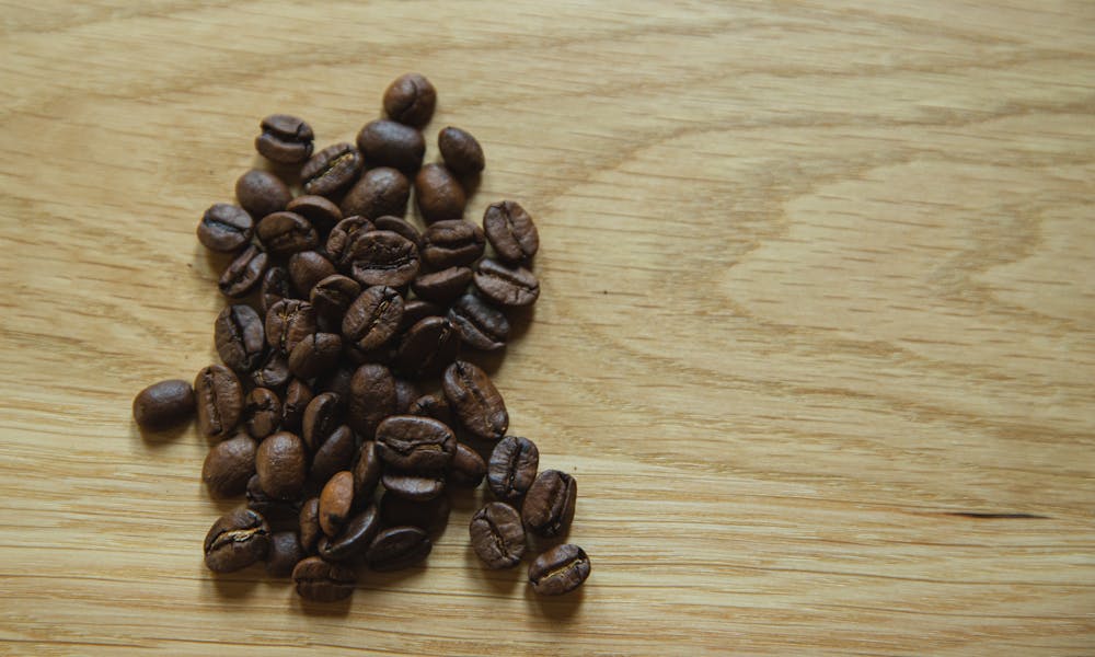 Top view of scattered coffee beans placed on wooden table before making coffee .pexels