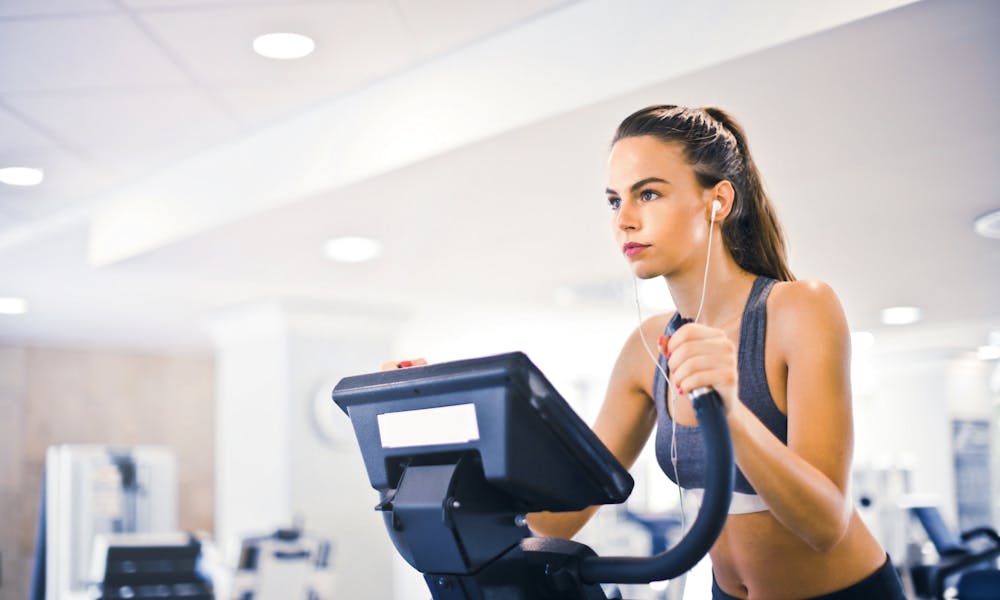 Serious fit woman in earphones and activewear listening to music and running on treadmill in light contemporary sports center .pexels
