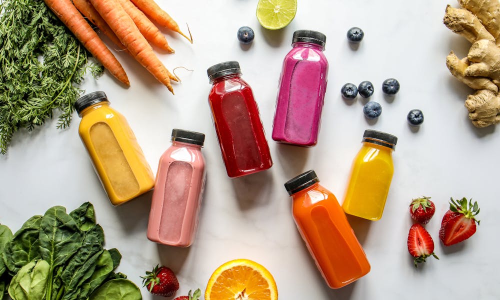 Colorful Bottles with Smoothies Beside Carrots, Ginger, Leaves and Berries .pexels
