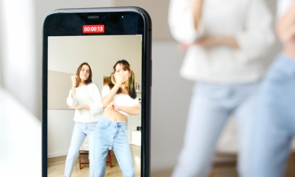 Woman in White Long Sleeve Shirt and Blue Denim Jeans Holding Black Iphone 5 .pexels