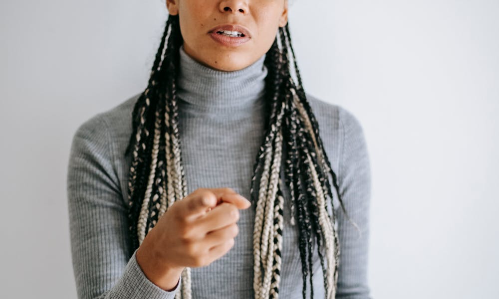 Ethnic female with long braids blaming  pointing with forefinger at camera standing against gray background .pexels