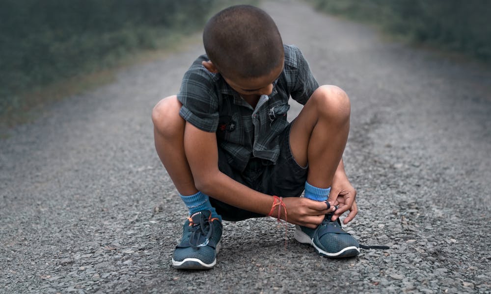 A young boy is kneeling on the road with his shoes .pexels