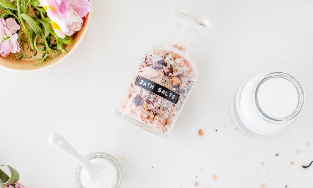Top view of fresh delicate Brompton stock flowers with pink petals placed on white table with various jars of bath salts .pexels