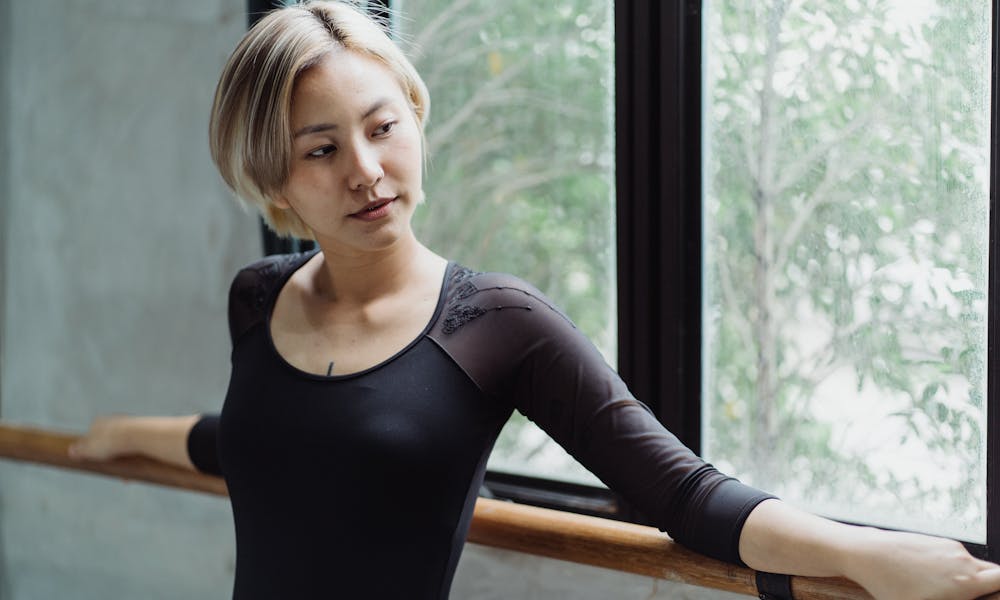 Concentrated young ethnic female dancer doing barre exercise near window in studio .pexels