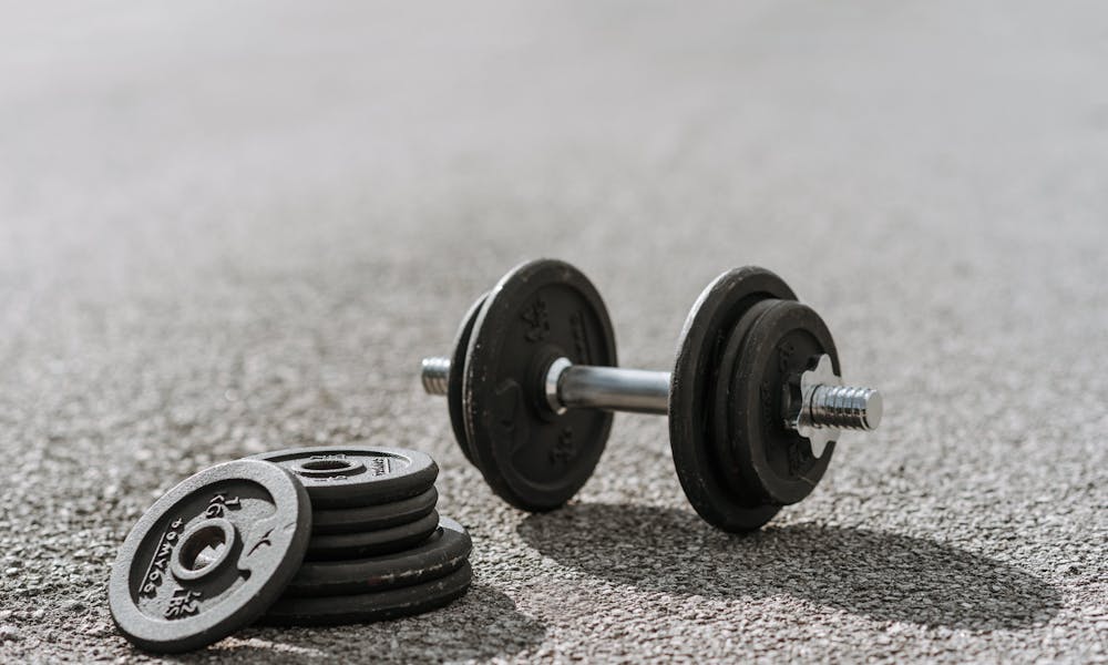 Dumbbell near pile of plates on pavement in sunlight .pexels