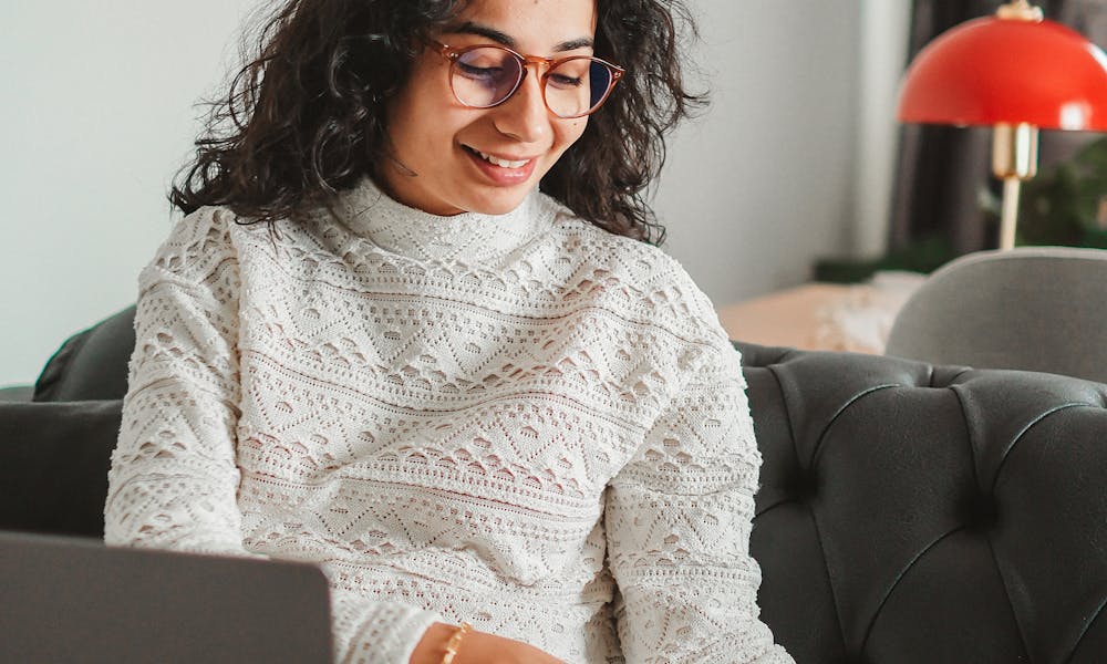 Young Woman with a Laptop on Her Lap Reaching for a Book .pexels