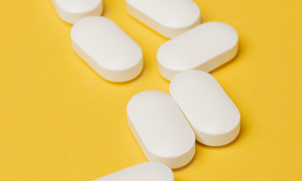 Heap of white pills on yellow surface .pexels