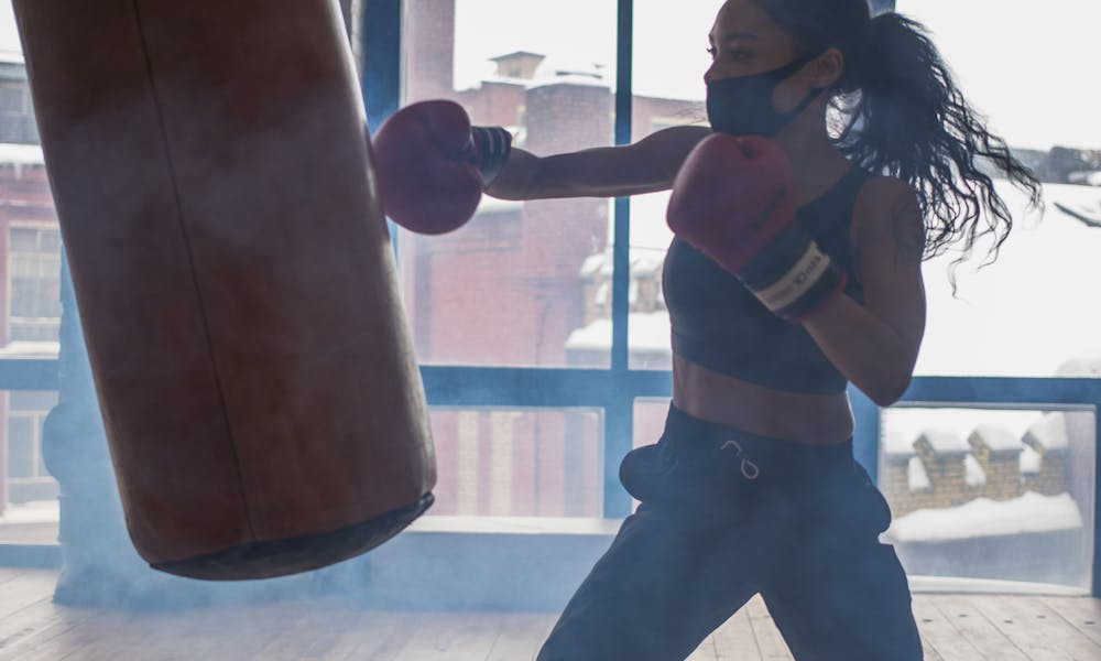 Active black boxer punching heavy bag while exercising in gymnasium .pexels