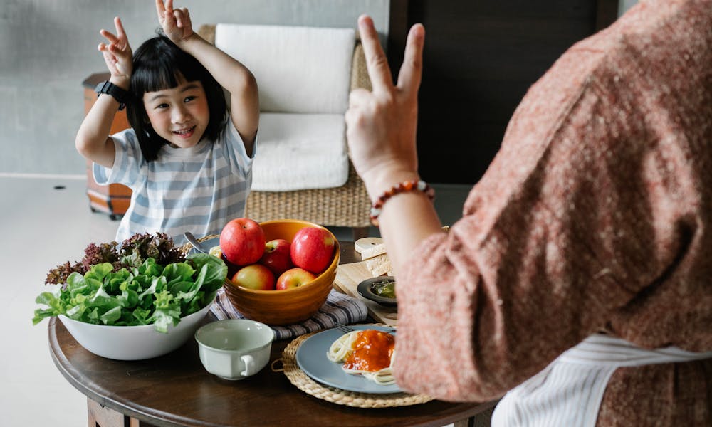 Happy little ethnic girl having fun with faceless mother showing V sign during lunch .pexels