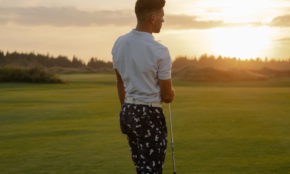 A golfer walking on a lush green course holding a club during a beautiful sunset. .pexels