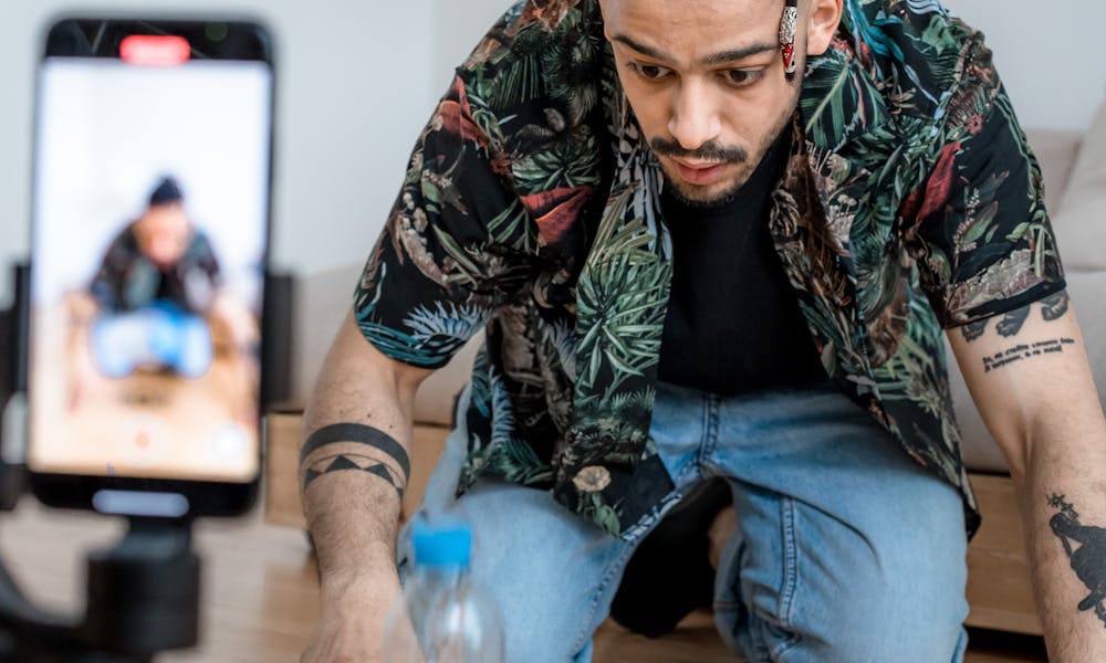A man filming a bottle flip challenge on a smartphone indoors, capturing a trending social media moment. .pexels