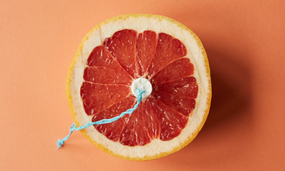 Artistic depiction of menstrual theme with grapefruit and tampon on orange background. .pexels