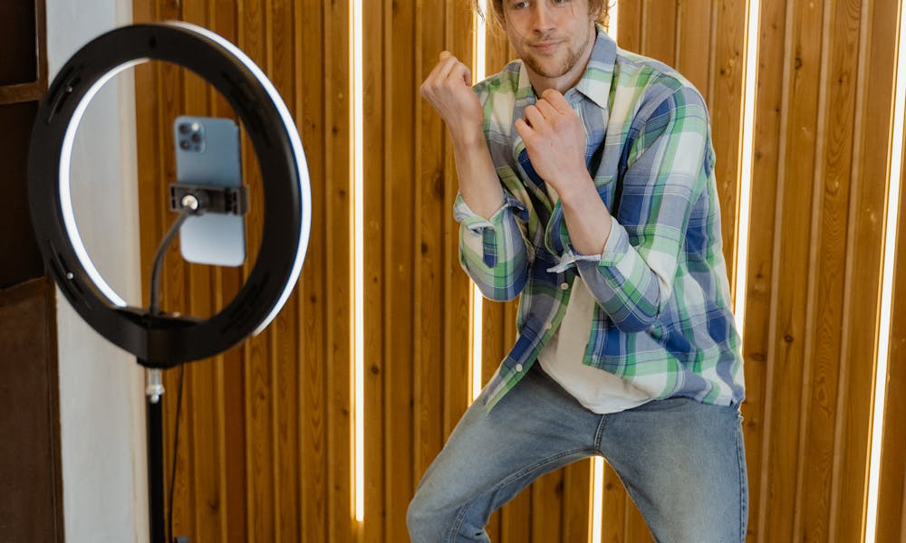 A young man dancing and posing in front of a smartphone and ring light setup in a modern room. .pexels