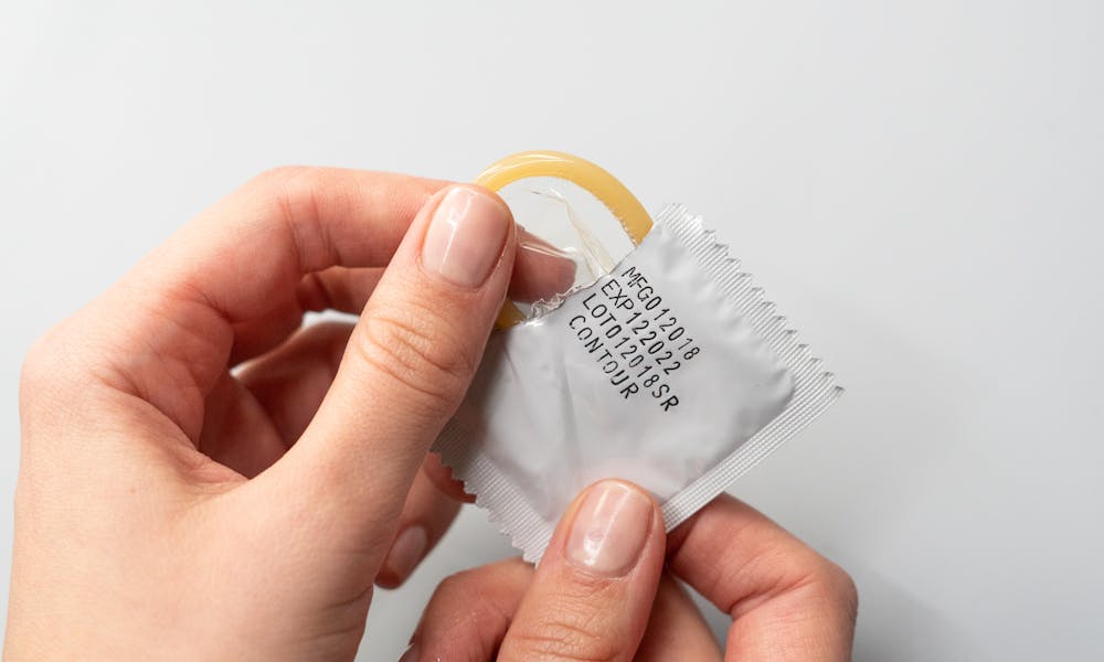 Close-up of hands opening a condom package, emphasizing safe sex and protection. .pexels