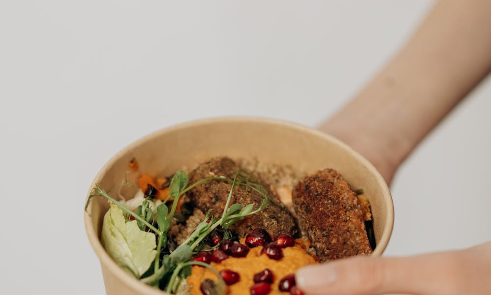 A hand holding a nutritious vegan bowl with fresh ingredients like greens and pomegranate seeds. .pexels
