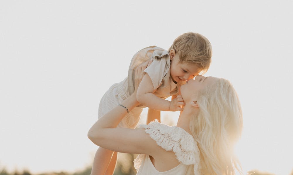 A serene moment of a mother embracing her child on a sunlit beach during sunset. .pexels