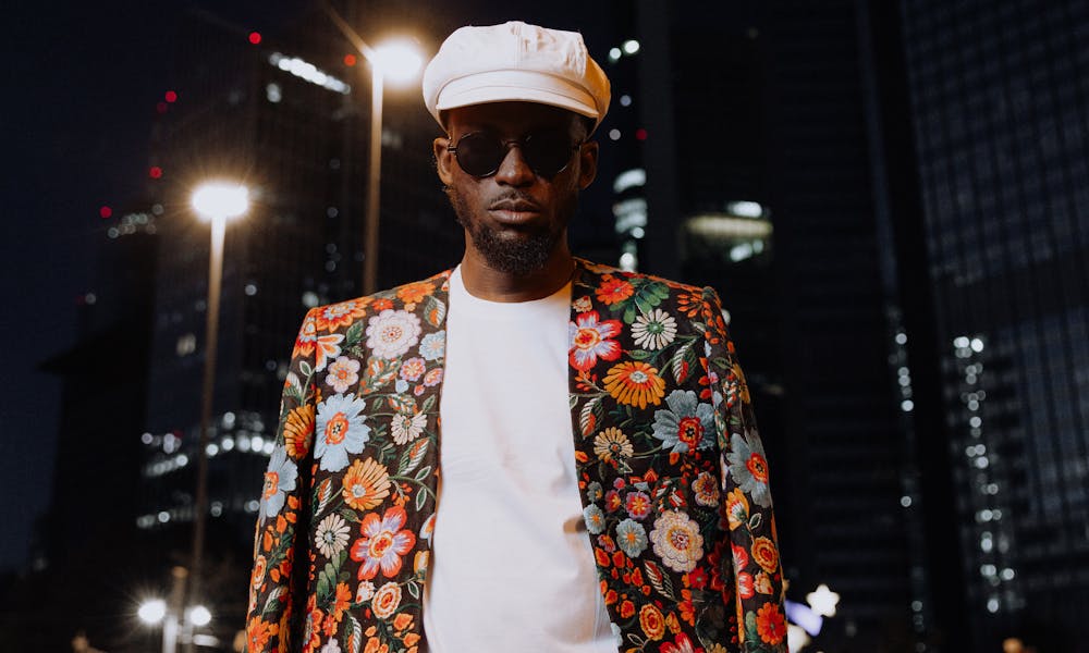 Man in floral jacket and orange pants poses in city at night, embodying urban fashion. .pexels