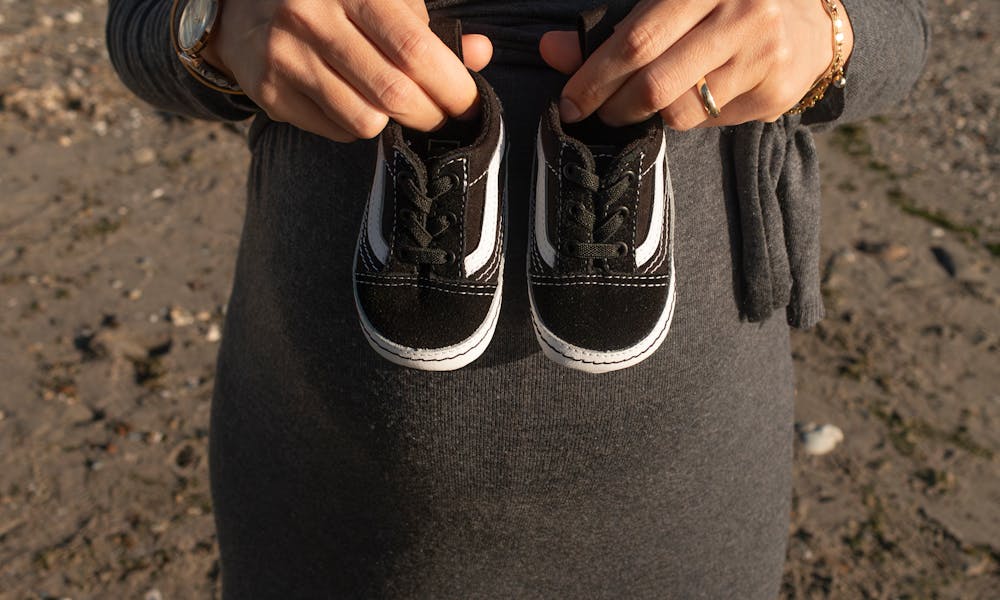 Expectant mother holding baby shoes near the ocean, symbolizing anticipation and joy. .pexels