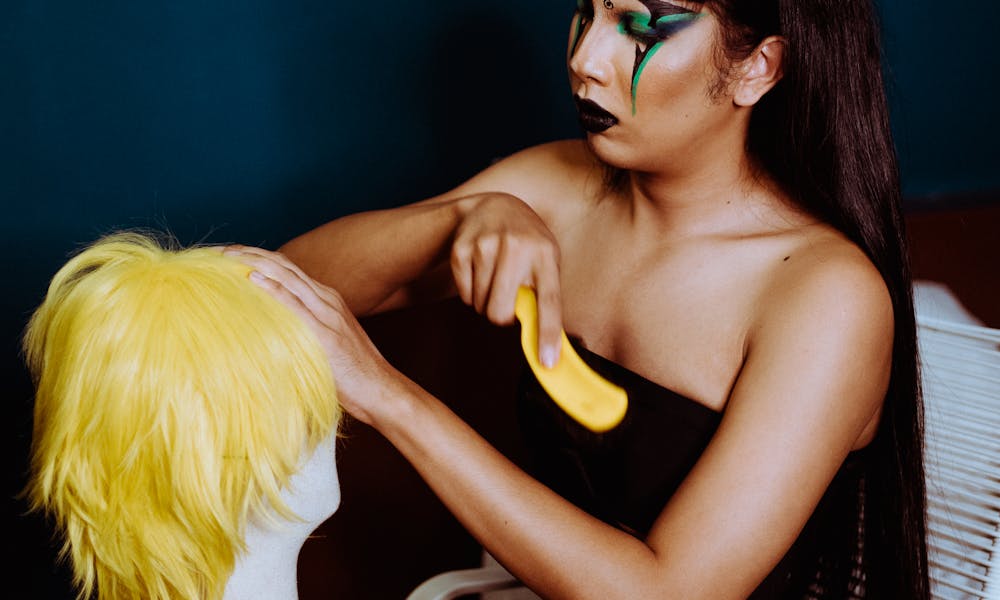 A makeup artist focuses intently on styling a vibrant yellow wig indoors. .pexels