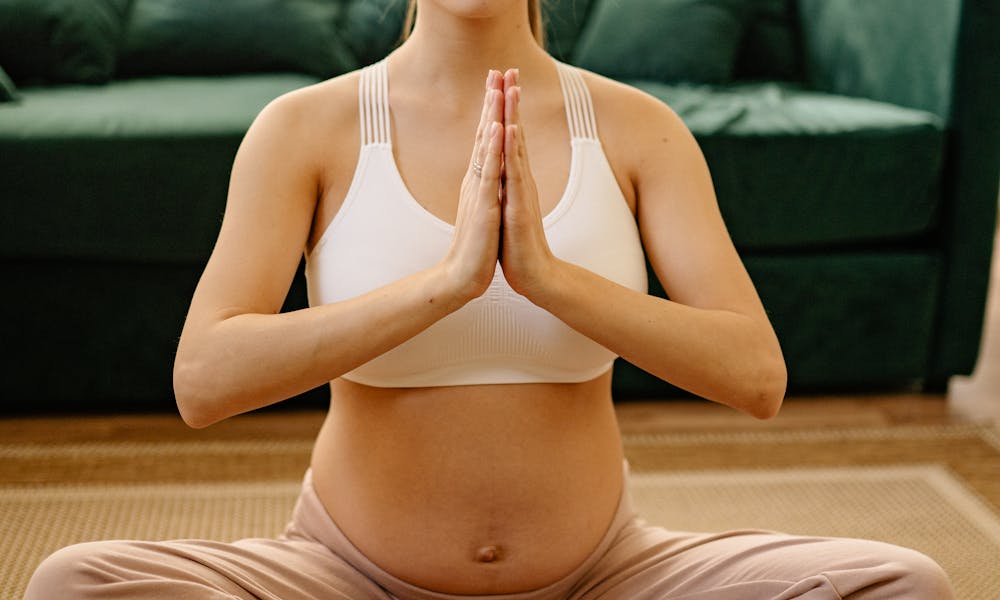 Serene pregnant woman meditating in lotus position at home, focusing on mindfulness and wellbeing. .pexels