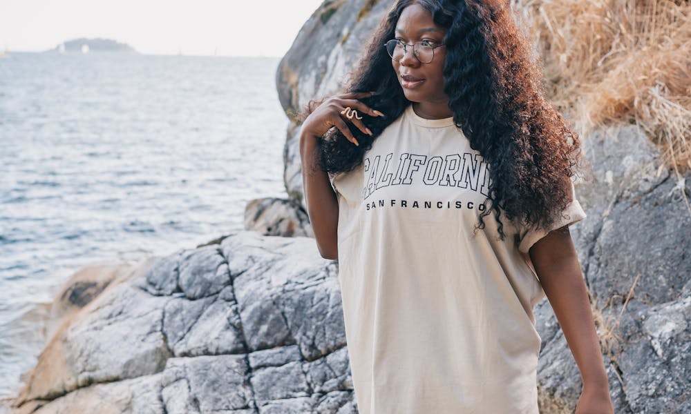 A woman in an oversized shirt stands beside rocky beach as she gazes into the distance. .pexels