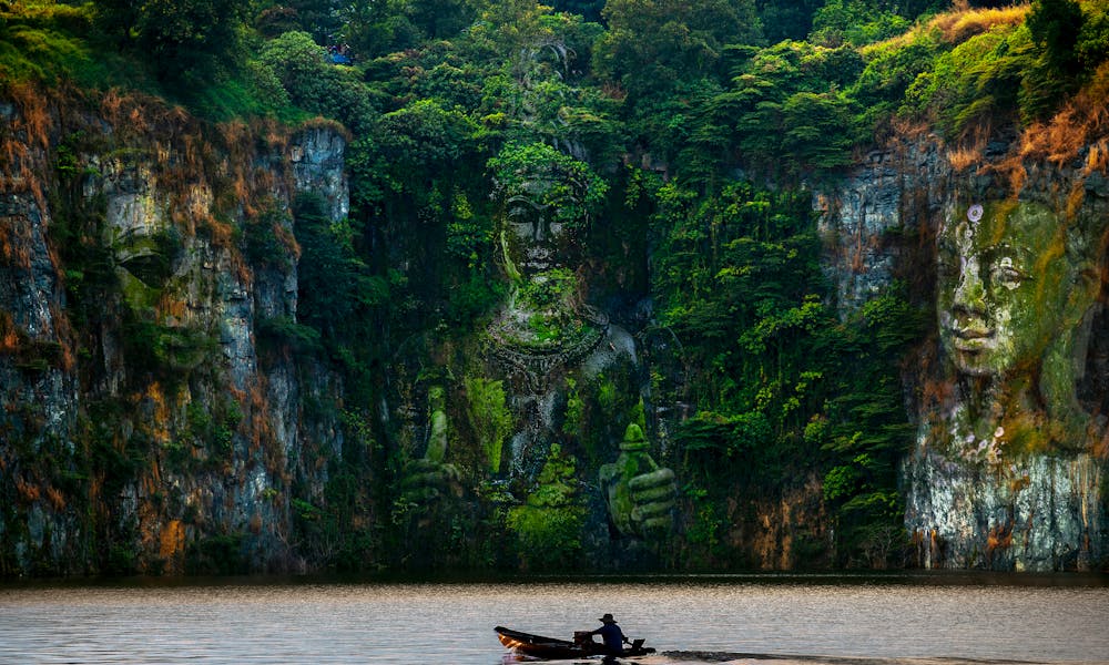 Ancient sculptures carved into a cliffside, reflected in the serene river below. .pexels