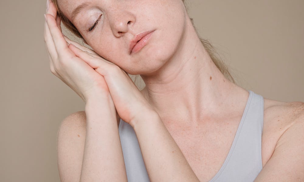 Woman with closed eyes in a serene pose, hands rested on face, studio setting. .pexels