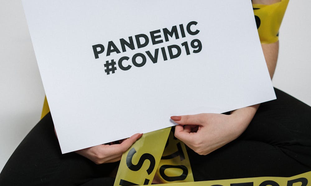 Person wrapped in caution tape holding a sign with COVID-19 awareness message. .pexels