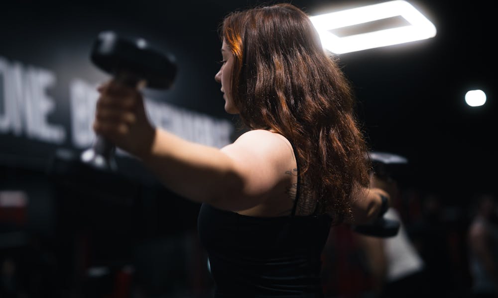 Side view of a woman exercising with dumbbells in a gym under bright lighting. .pexels