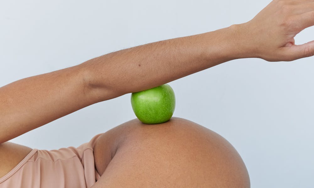 Creative portrayal of pregnancy with a green apple and arm in studio setting. .pexels