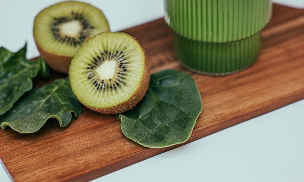 Close-up of a kiwi spinach smoothie in a ribbed glass on a wooden board with sliced kiwi and leaves. .pexels