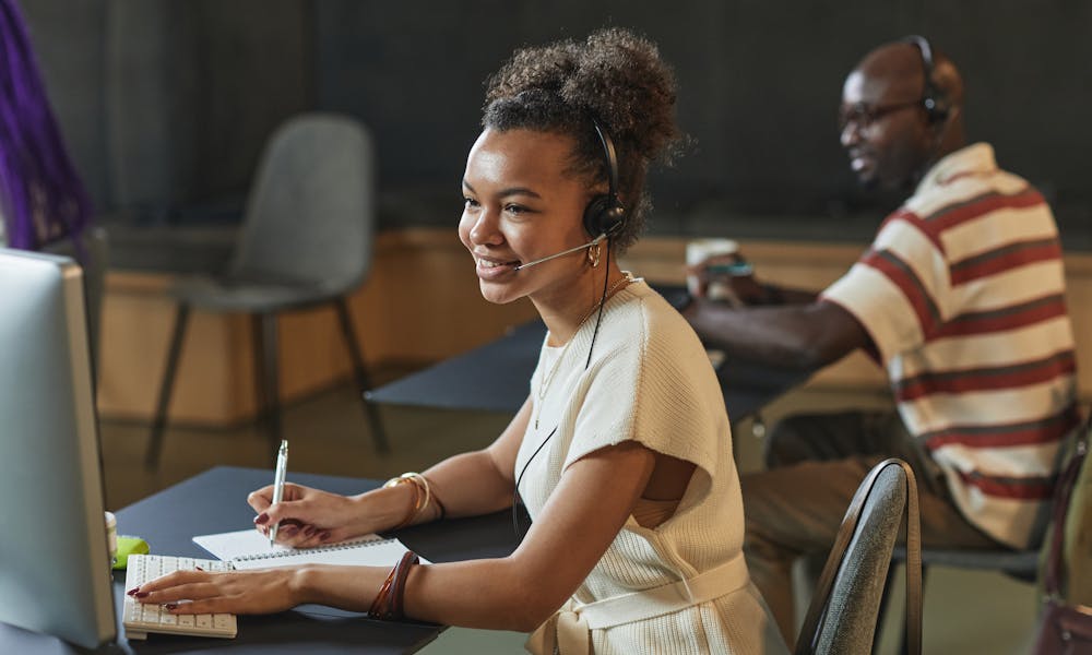Cheerful woman in a call center using a headset and computer while working. .pexels