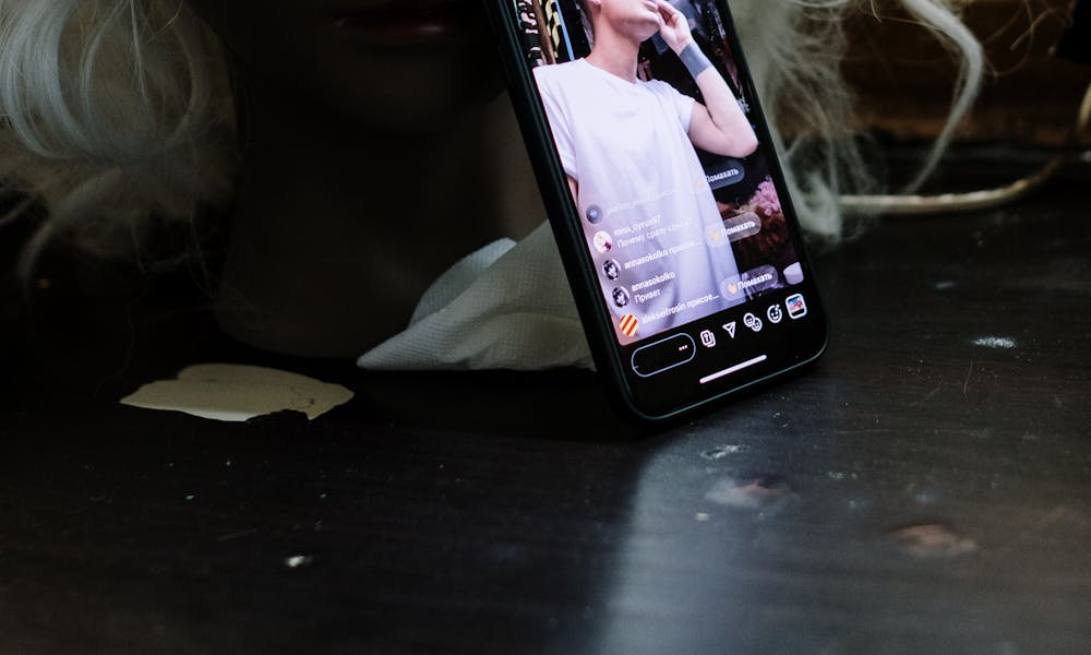 Close-up of a mannequin with a smartphone displaying a live makeup stream in a dim indoor setting. .pexels