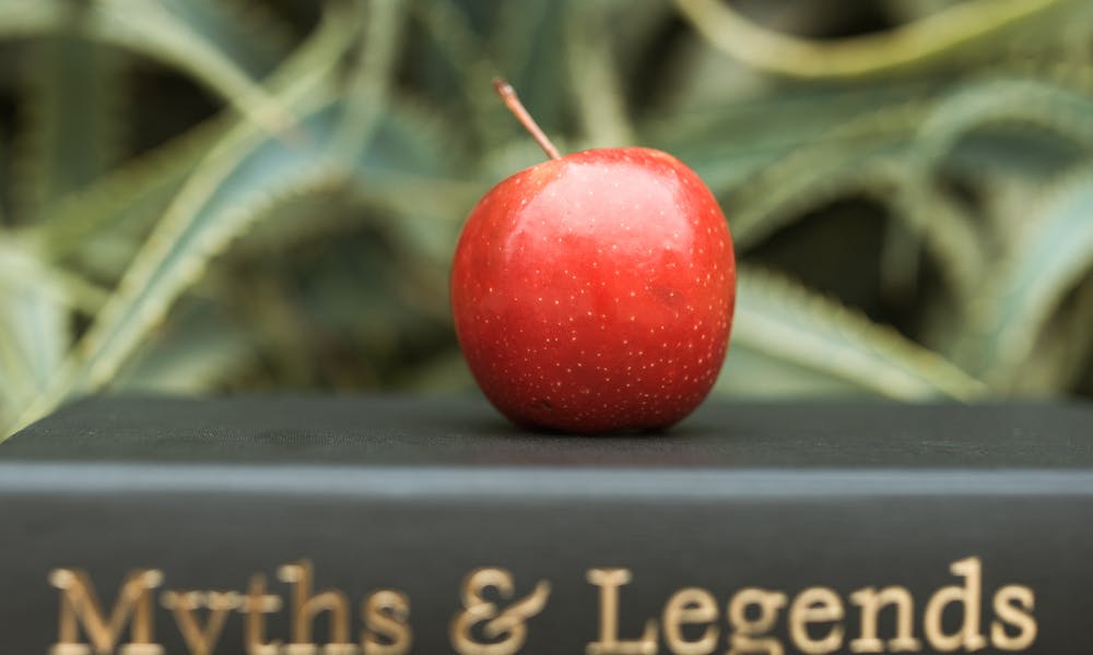 Red apple placed atop a 'Myths & Legends' book against an abstract background, representing knowledge and temptation. .pexels